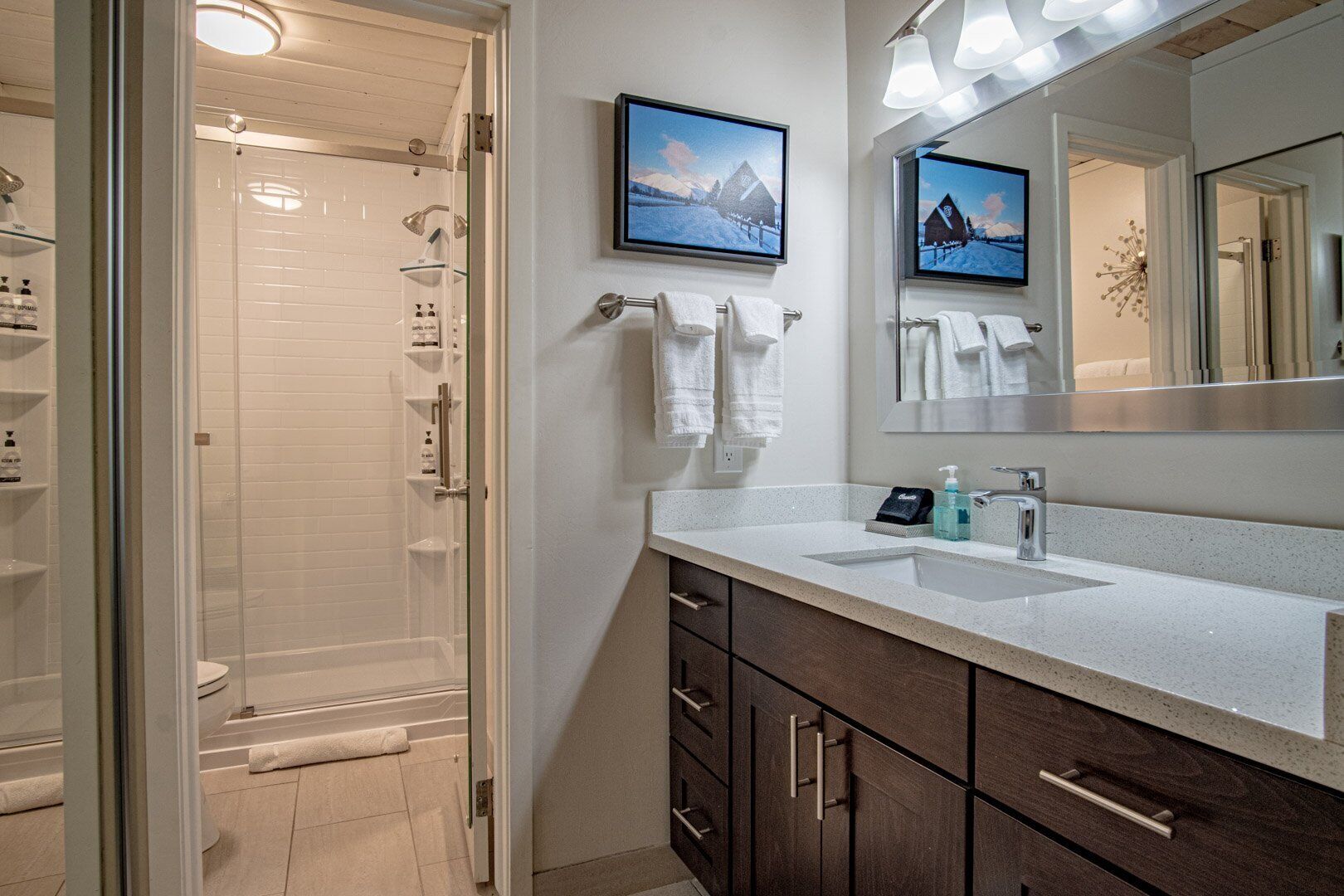 A modern bathroom with a glass shower enclosure, a large mirror, and a countertop with a sink and toiletries.
