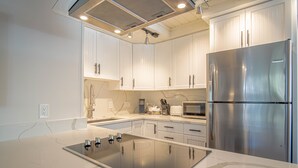 A modern kitchen with white cabinets, a stainless steel refrigerator, and an induction cooktop. - Atelier Allure - 2BD Mountain View + Free Resort Amenities (Sun Valley)