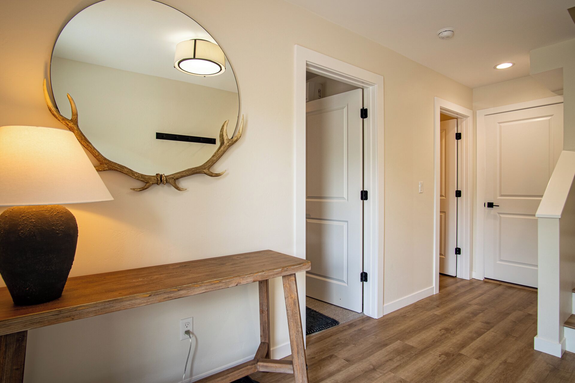 Un couloir avec une console en bois, un miroir rond orné de motifs de bois de cerf et des portes blanches.