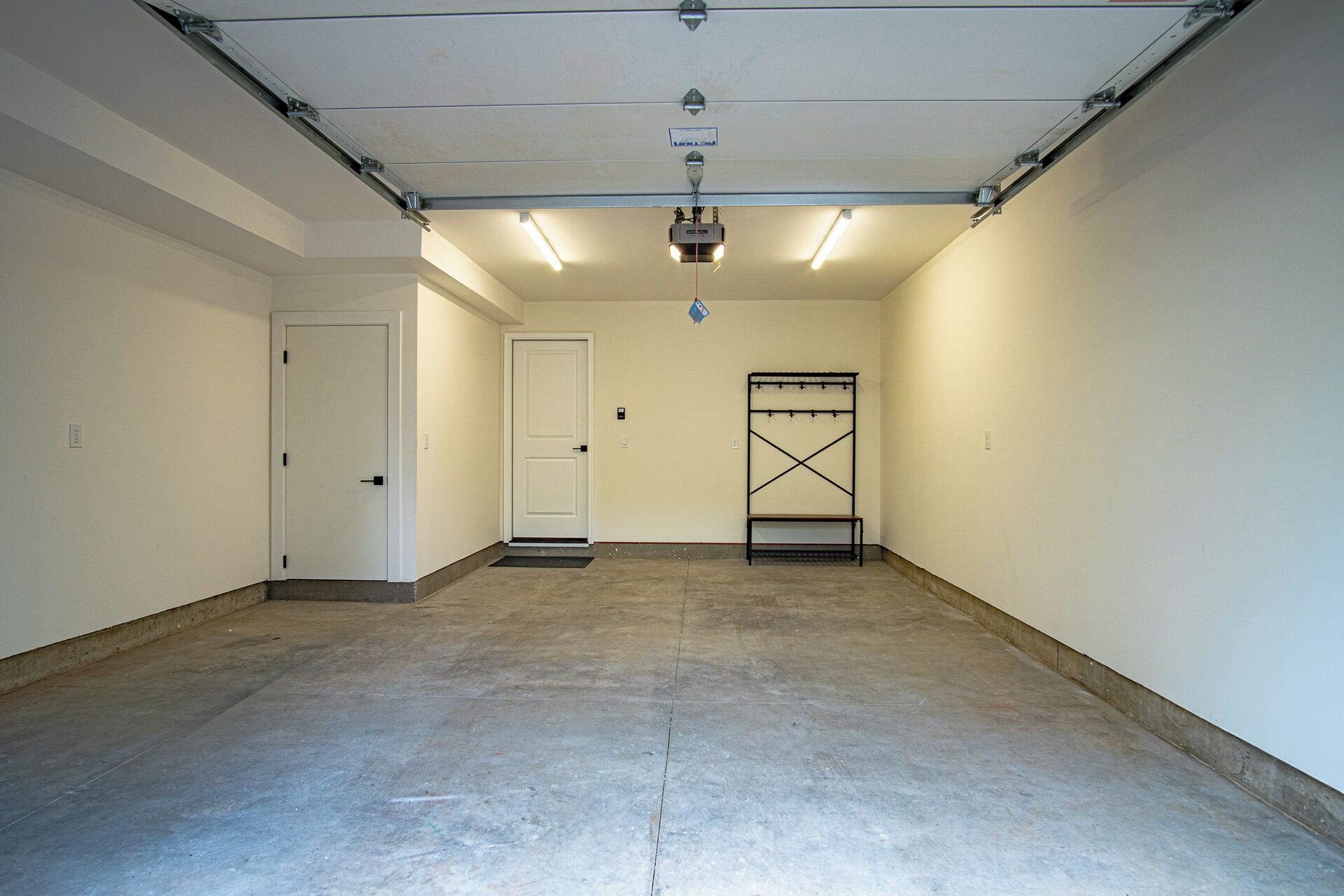 A clean, empty garage with a concrete floor, white walls, and a ceiling with fluorescent lighting.