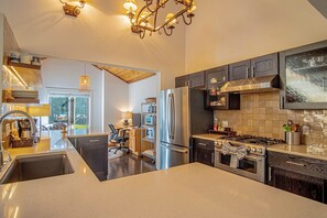 A modern kitchen with stainless steel appliances, a large island, and a dining area with a view. - Panoramic Views! Designer`s Condo on Golf Course W/resort Amenities (Sun Valley)