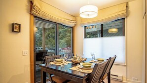 A dining area with a wooden table set for four, a window with blinds, and a hanging light fixture. - Sv139 - Walk to Lifts & Town - Hot Tub & Pool (Ketchum)