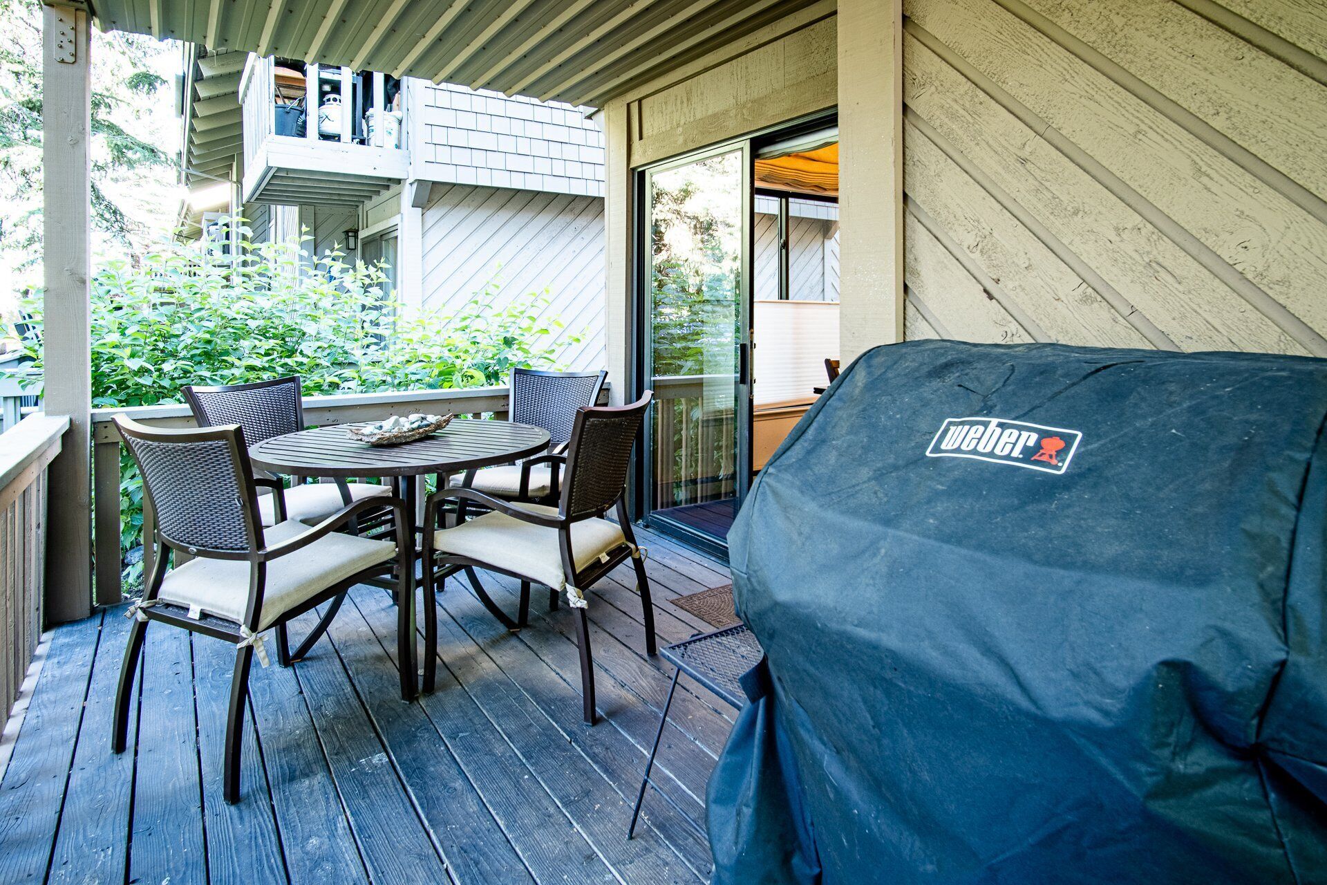 A covered patio with a grill, outdoor seating, and a view of the house.