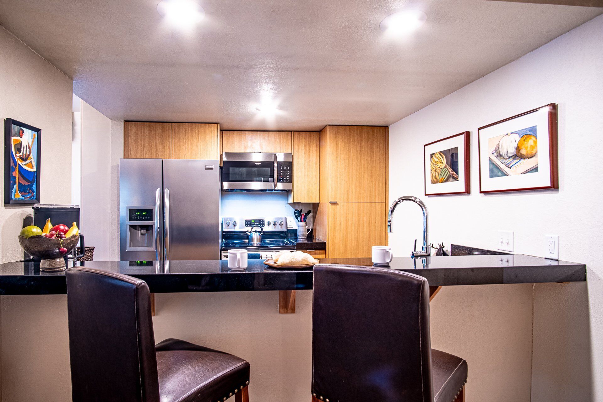 Una cocina compacta con electrodomésticos de acero inoxidable, armarios de madera y una isla central con taburetes de bar.