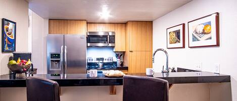 Una cocina compacta con electrodomésticos de acero inoxidable, armarios de madera y una isla central con taburetes de bar.