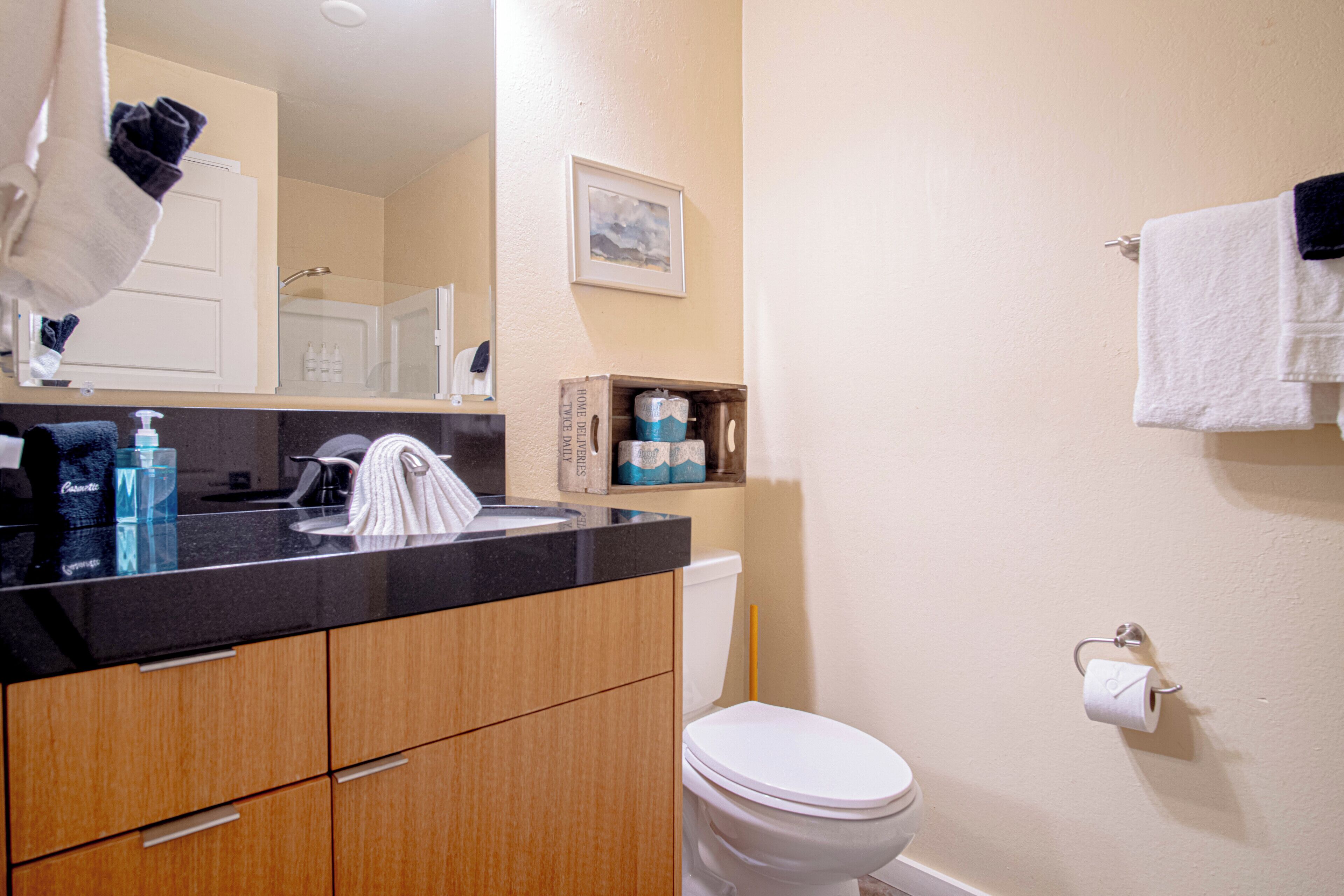 A bathroom with a toilet, sink, and wooden cabinets. There is a towel rack with towels, a picture on the wall, and a toilet paper holder.