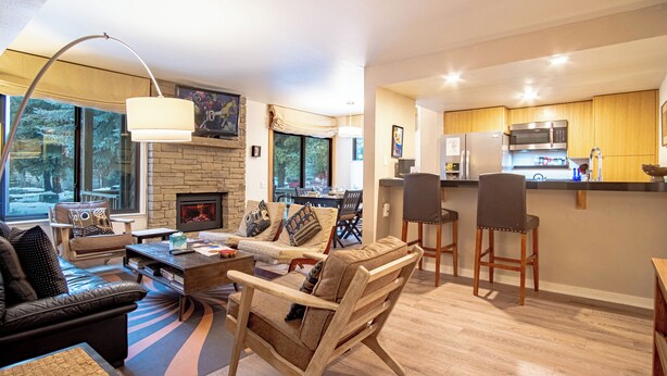 A modern living room with a fireplace, seating area, and a kitchen with wooden cabinets and a microwave. - Sv139 - Walk to Lifts & Town - Hot Tub & Pool (Ketchum)