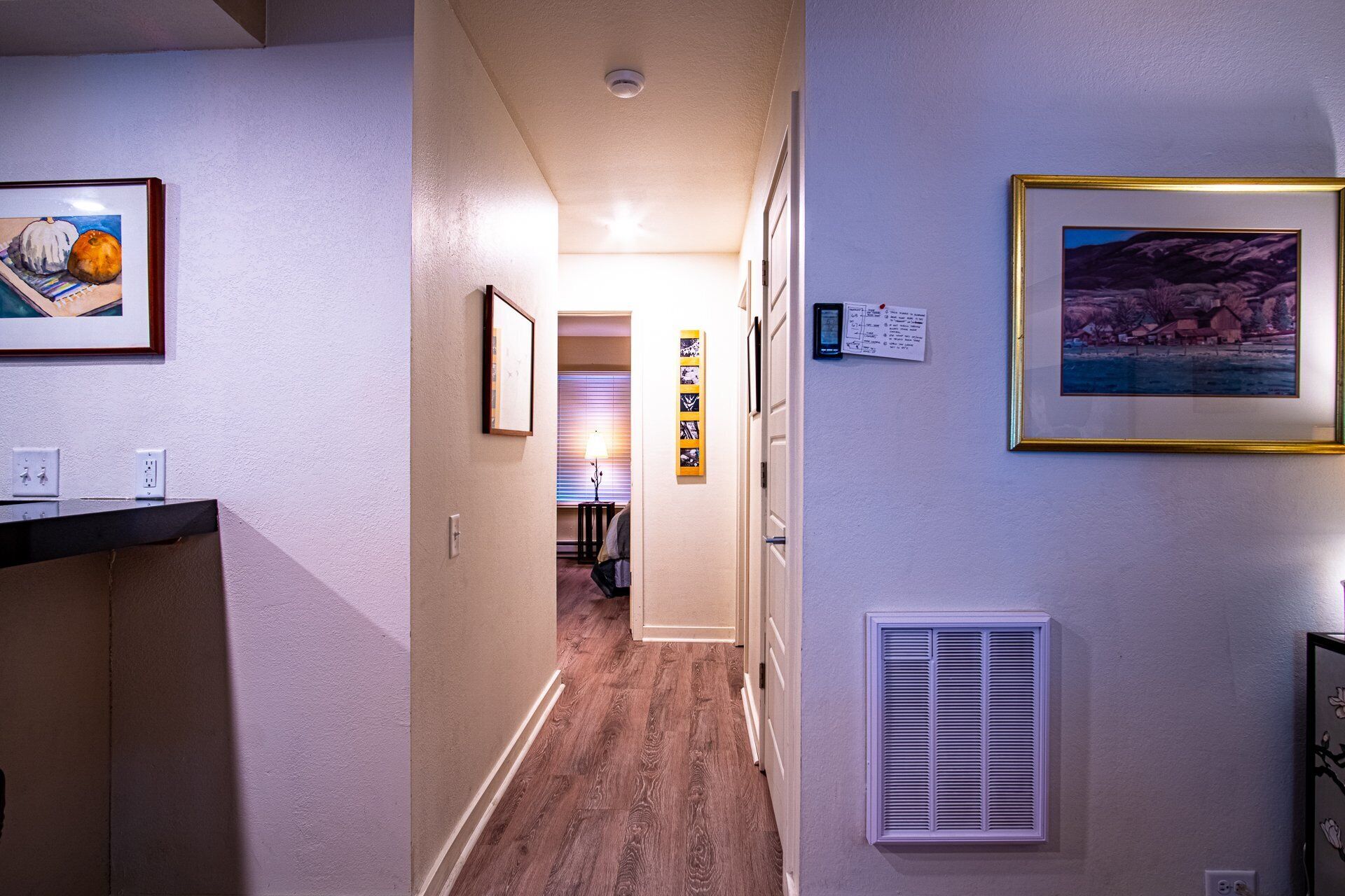 A hallway with a wooden floor, a door at the end, and framed pictures on the walls.