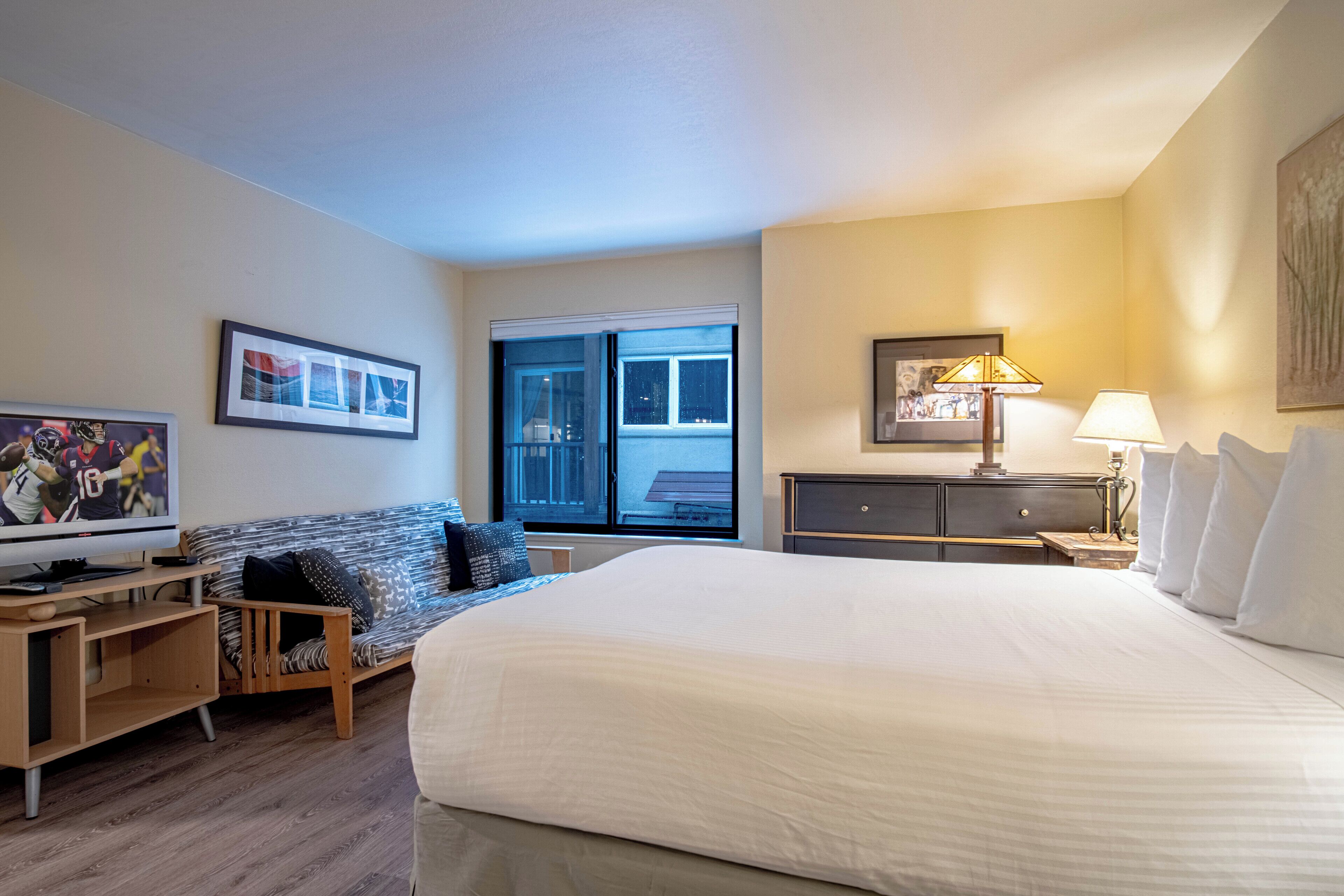 A hotel room with a large bed, a TV, a sofa, and a desk.