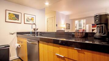 A modern kitchen with wooden cabinets, a stainless steel dishwasher, a black countertop, and a coffee maker.