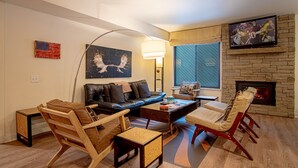 A living room with a sofa, chairs, a coffee table, a TV, a fireplace, and a flag on the wall. - Sv139 - Walk to Lifts & Town - Hot Tub & Pool (Ketchum)