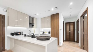 A modern kitchen with a central island, white cabinetry, and a wooden door in the background. - StayShort - Canal View 2BR in the Heart of Business Bay - Sleeps 6! (Business Bay)