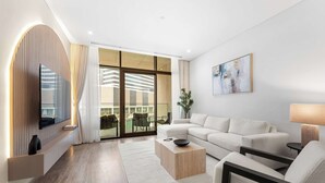A modern living room with a sofa, coffee table, and TV mounted on a wall. - StayShort - Canal View 2BR in the Heart of Business Bay - Sleeps 6! (Business Bay)