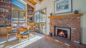 A cozy living room with a fireplace, a dining area with a table and chairs, and a bookshelf filled with books and decorative items. - Sv120 - Walk to Lifts & Town - Hot Tub & Pool (Ketchum)