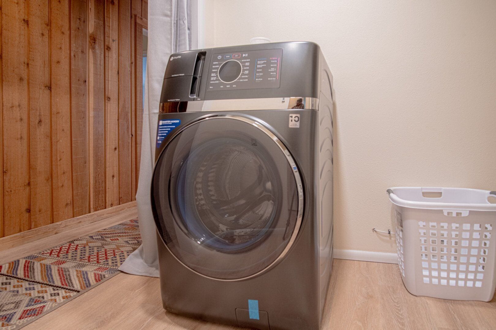 A front-loading washing machine in a room with wooden flooring and a patterned rug.