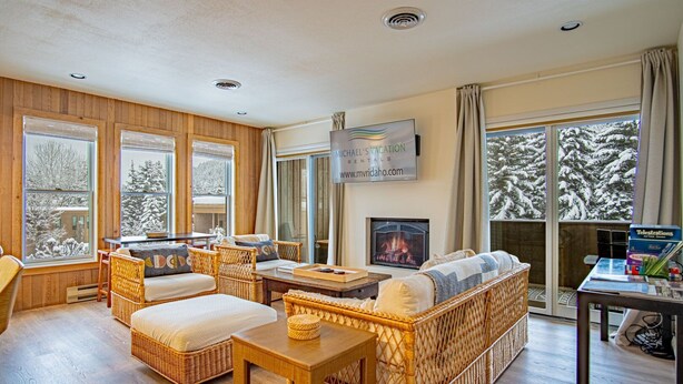 Ein gemütliches Wohnzimmer mit Korbmöbeln, einem Kamin und großen Fenstern mit Blick auf Schnee.