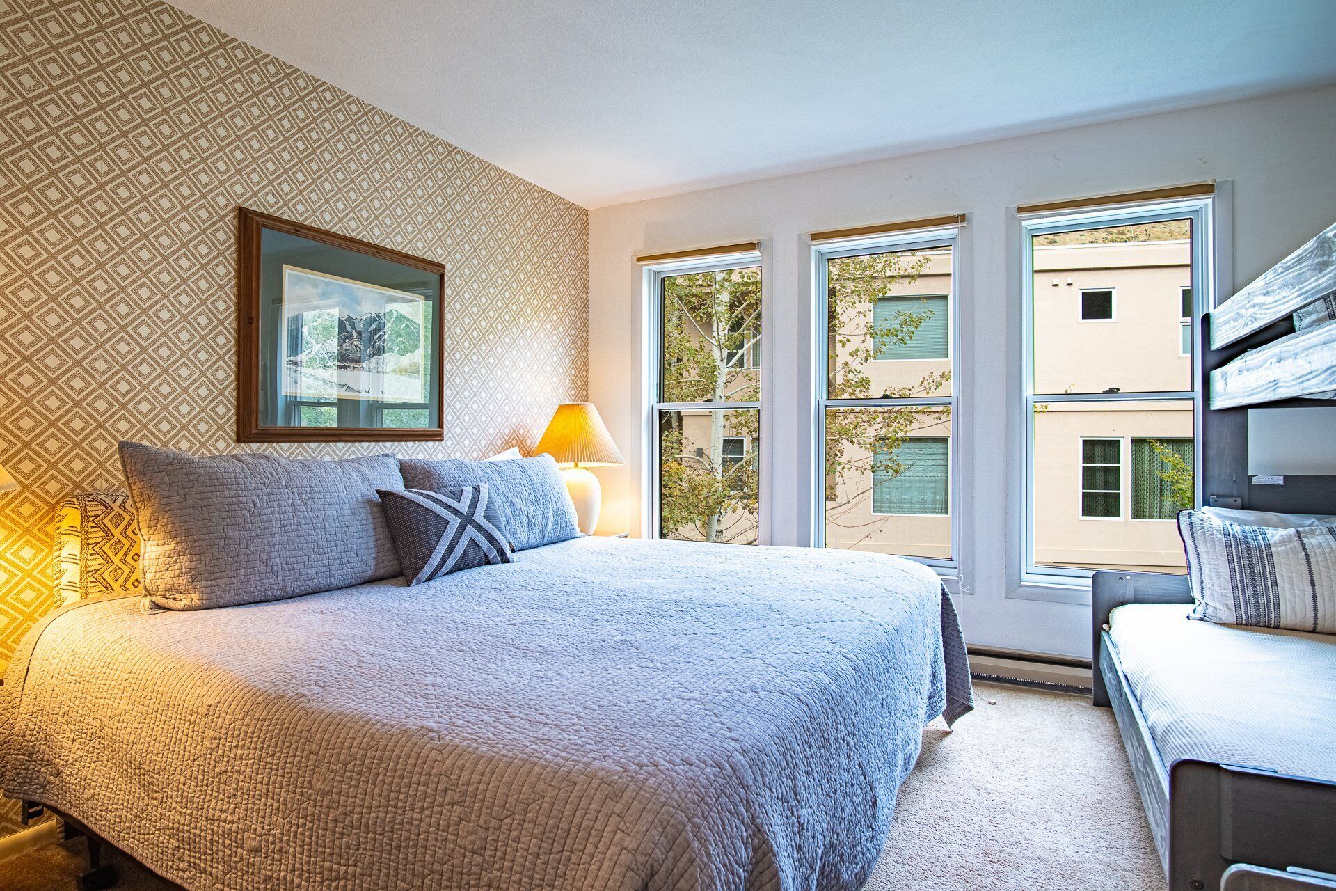 Un dormitorio con una cama grande, un escritorio y una ventana que ofrece vistas a edificios.