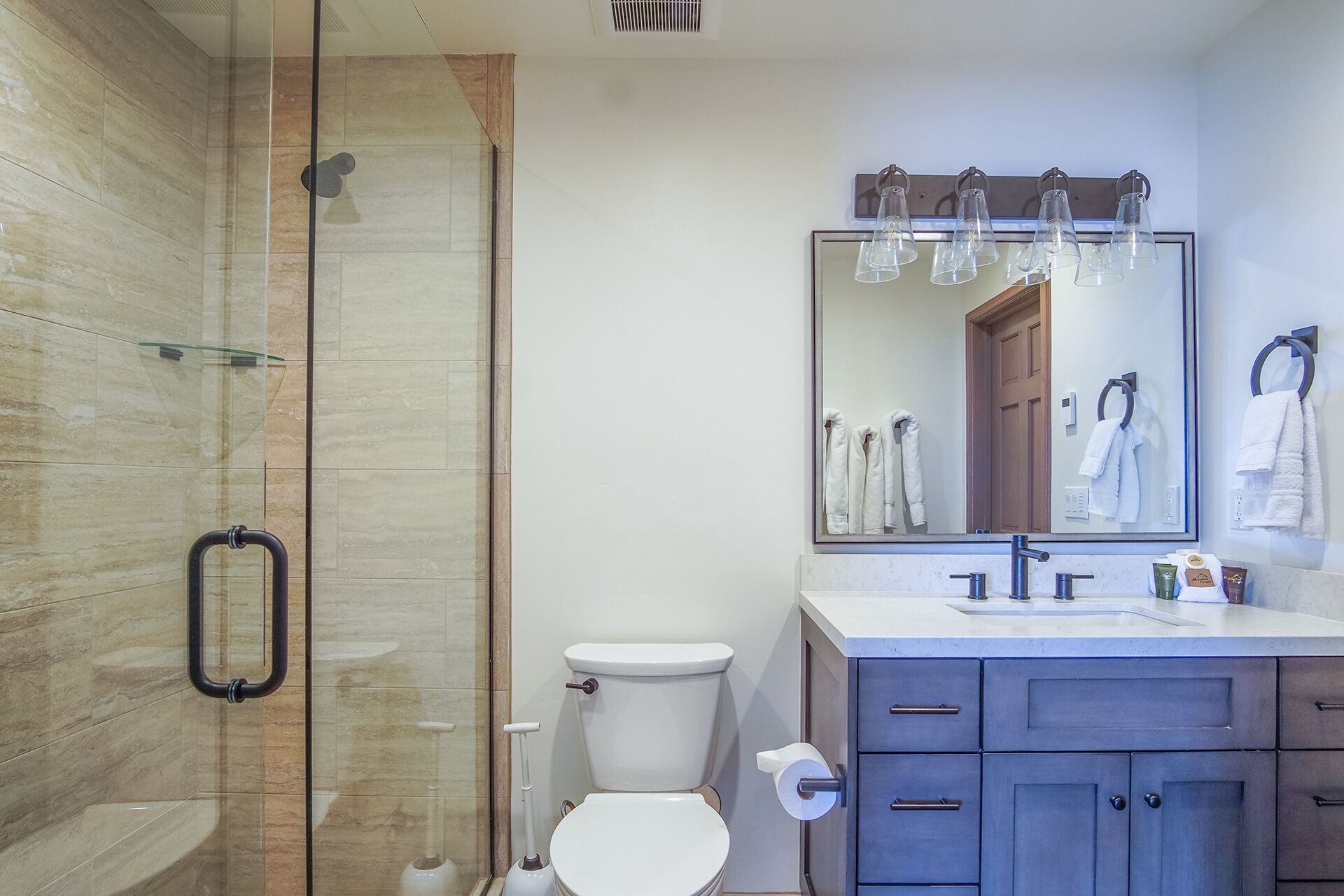 Un bany modern amb una cabina de dutxa de vidre, un vàter, un lavabo amb mirall i un penjador de tovalloles.
