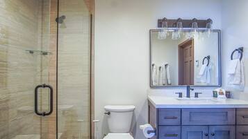 Un bany modern amb una cabina de dutxa de vidre, un vàter, un lavabo amb mirall i un penjador de tovalloles.