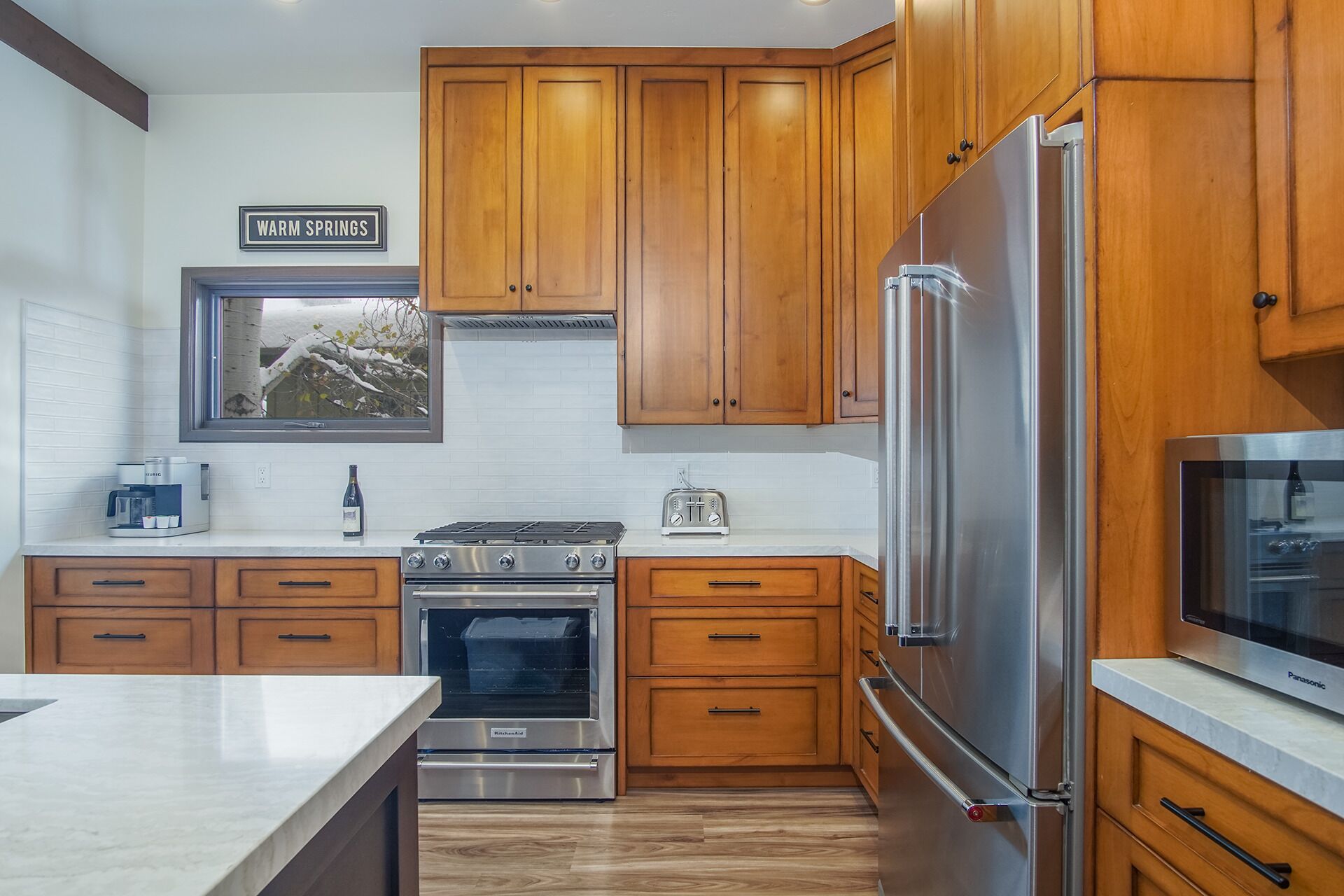 A modern kitchen with wooden cabinets, a stainless steel refrigerator, a built-in oven, and a coffee maker.