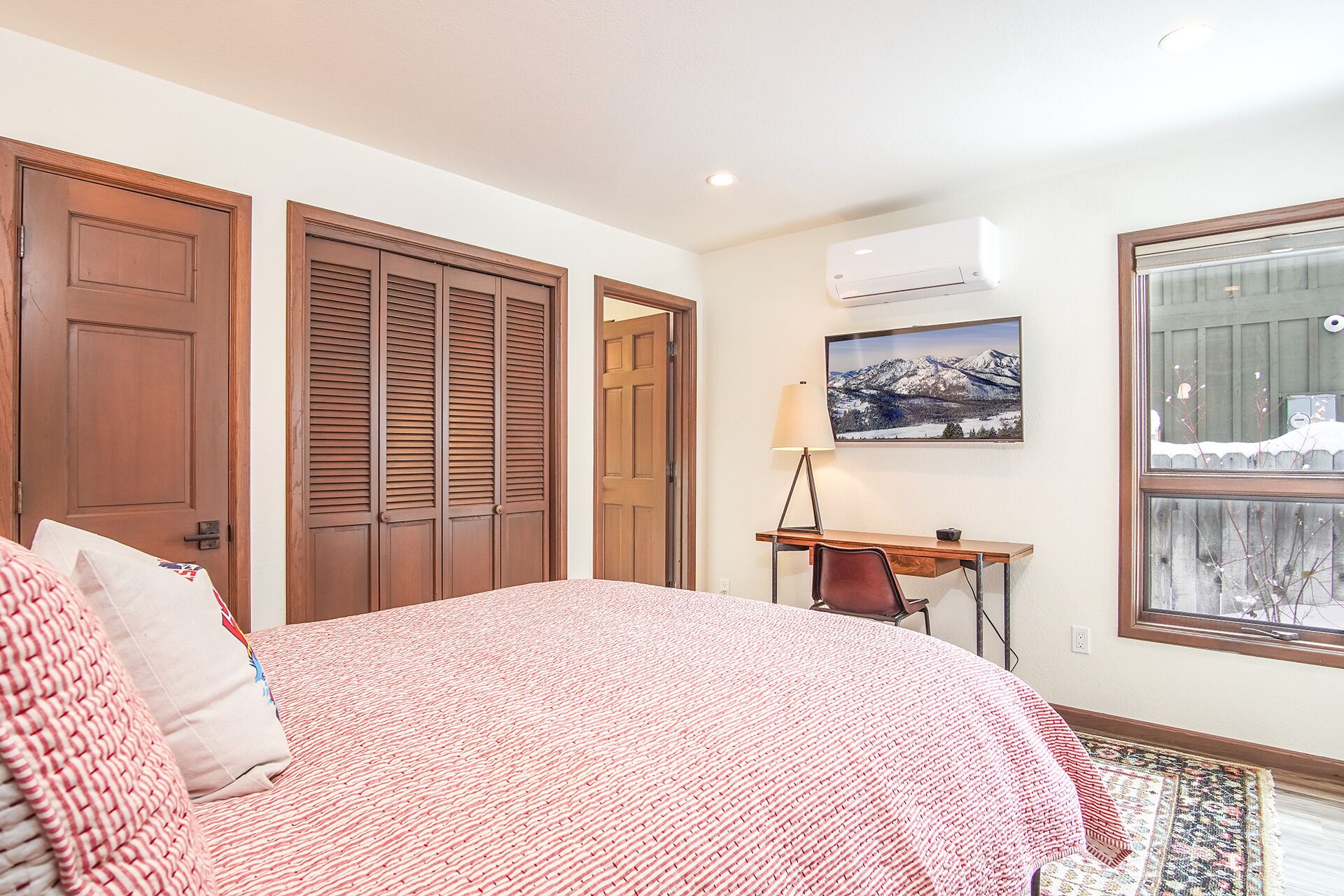 Une chambre dotée d’un grand lit, de portes en bois, d’un appareil de climatisation, d’un bureau avec une chaise et d’une fenêtre donnant sur les montagnes.