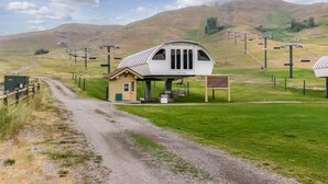 Un bâtiment unique et moderne, doté d’un toit incurvé et de grandes fenêtres, situé dans un paysage rural, avec des collines et des lignes électriques en arrière-plan.