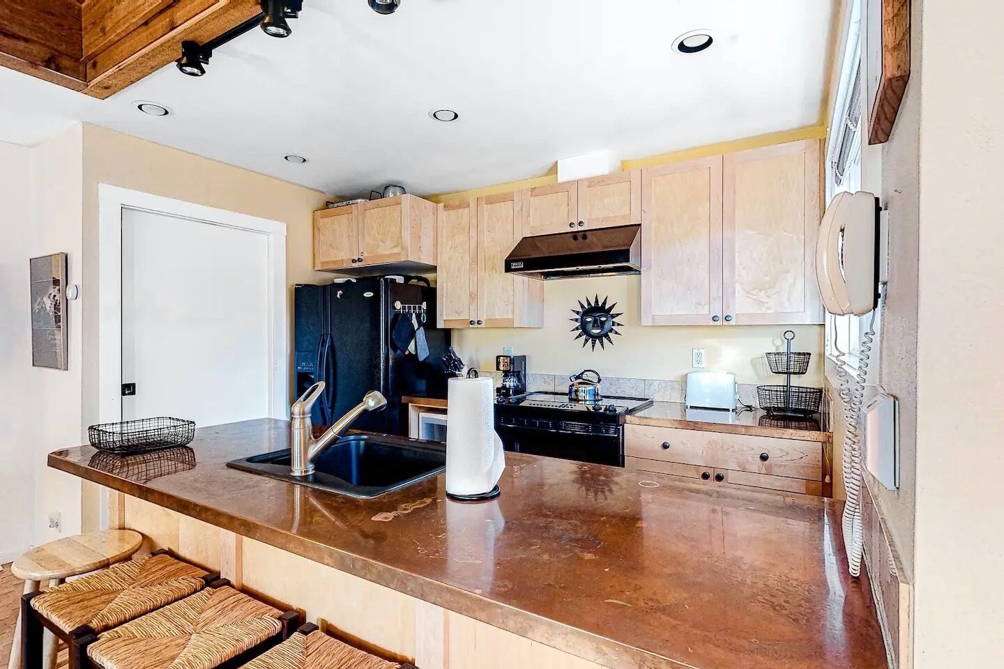 A kitchen with wooden cabinets, a black refrigerator, a sink, and a stove.
