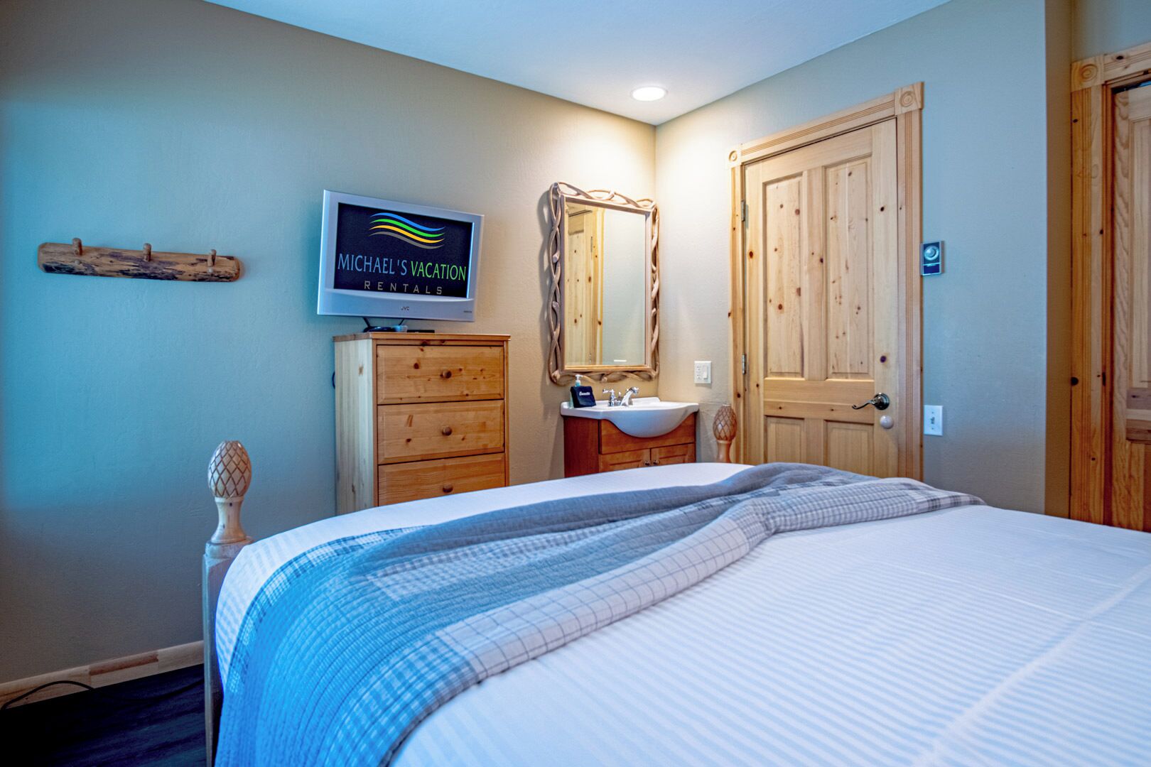 Un dormitorio con una cama, televisión, cómoda de madera, espejo y puerta.