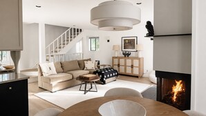 A modern living room with a sofa, a dining table with a bowl, a fireplace, and a staircase. - Indian Springs Oasis - Near Ski Slopes & Resort Amenities (Sun Valley)