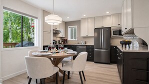 A modern kitchen with a dining area, stainless steel appliances, and a view of greenery outside. - Indian Springs Oasis - Near Ski Slopes & Resort Amenities (Sun Valley)