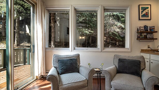 Um quarto acolhedor com duas poltronas, uma mesa pequena e uma janela com vista para árvores.