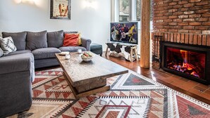 Uma sala de estar com sofá, mesa de centro, lareira, televisão e um quadro na parede.