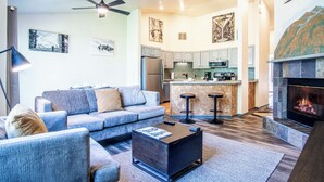 A modern living room with a sofa, coffee table, and fireplace. There is a kitchen area with a refrigerator and a microwave. - Della View 2BR Condo - In the Heart of Historic Downtown Hailey! (Hailey)