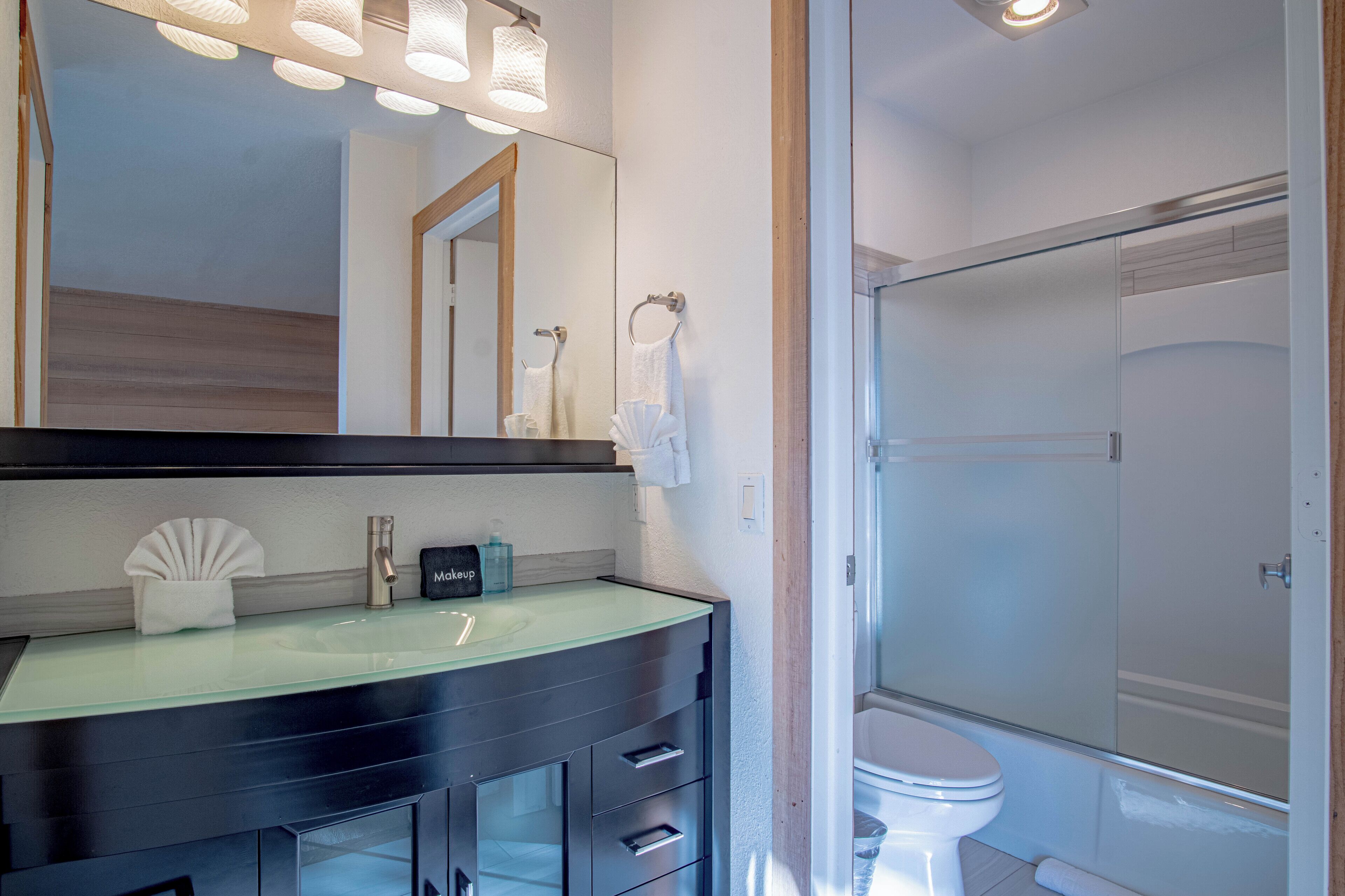 A modern bathroom with a glass shower enclosure, a vanity with a glass sink, and a large mirror.