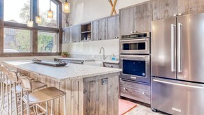 A modern kitchen with wooden cabinets, stainless steel appliances, and a large island with bar stools. - Snow Creek 1554 - Ski-in/ski-out + Pool & Hot Tub (Sun Valley)
