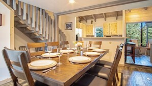 A dining area with a wooden table set for six, surrounded by chairs, and a staircase on the left. - Snow Creek 1554 - Ski-in/ski-out + Pool & Hot Tub (Sun Valley)