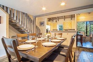 Un comedor con una mesa de madera dispuesta para seis personas, rodeada de sillas, y una escalera a la izquierda.
