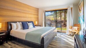 A modern bedroom with a large bed, wooden paneling on the walls, a view of the outdoors through a sliding glass door, and a chair by the window. - Snow Creek 1554 - Ski-in/ski-out + Pool & Hot Tub (Sun Valley)