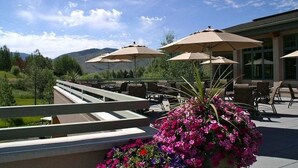 An outdoor patio area with beige umbrellas, outdoor seating, and a flower planter. - Elkhorn Springs Sanctuary - Pool/hot Tub/underground Parking (Sun Valley)