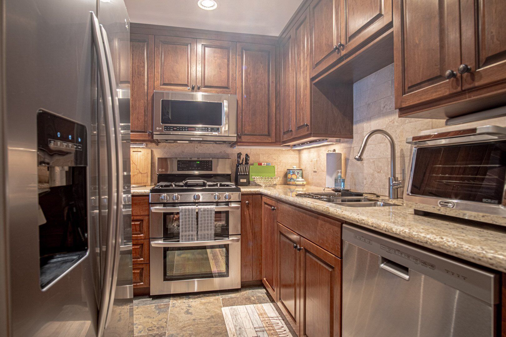 A compact kitchen with wooden cabinets, stainless steel appliances including a microwave, stove, oven, and dishwasher, and a granite countertop.