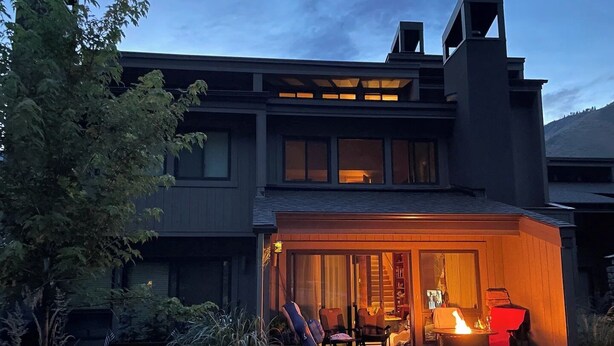 Ein modernes Haus mit überdachter Terrasse, einem Feuerkorb und Sitzgelegenheiten.