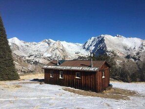 A wooden cabin with a metal roof, surrounded by snow-covered mountains and a clear blue sky. - Snow Creek 1553 - Ski-in/ski-out + Pool & Hot Tub (Sun Valley)
