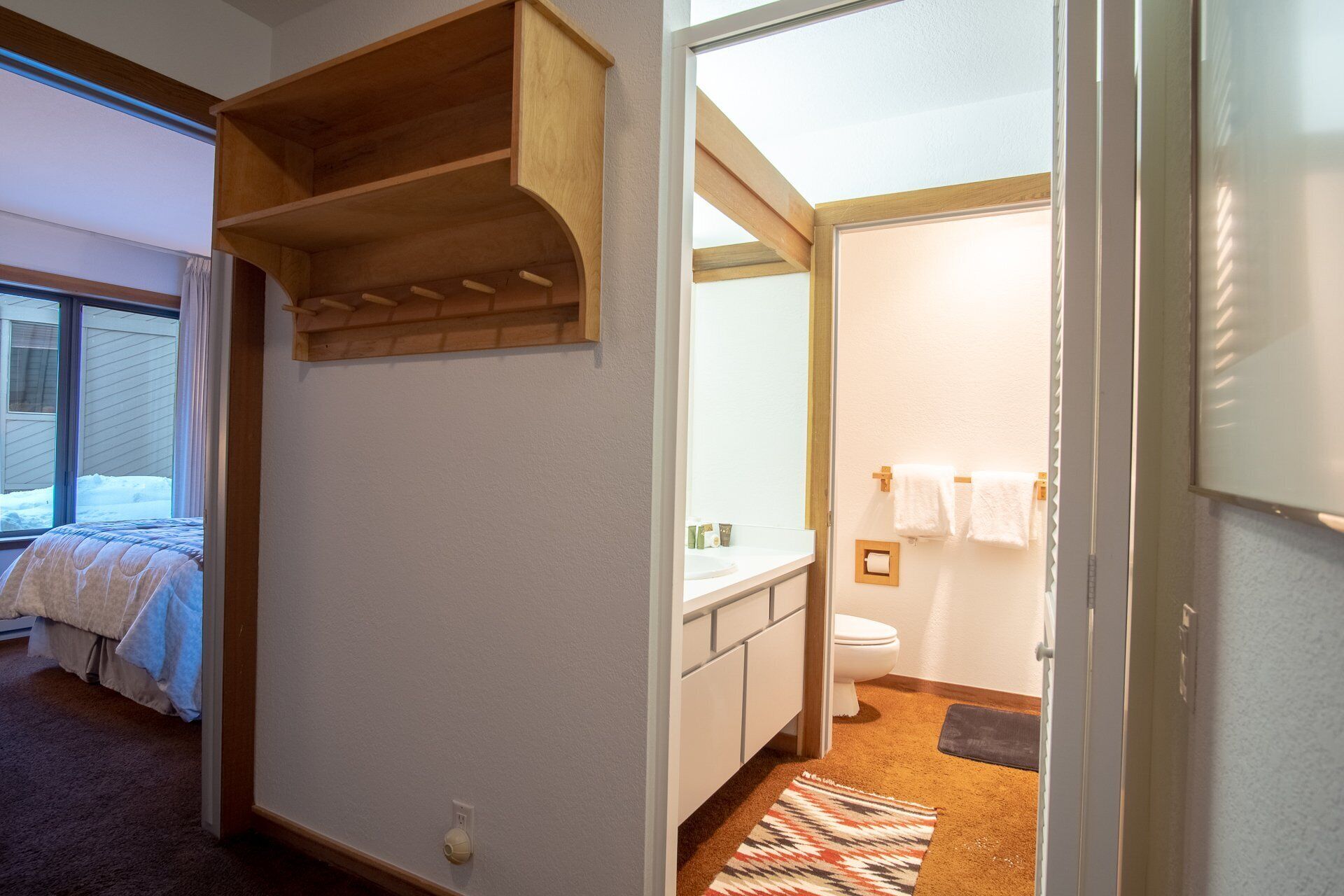 A bedroom with a bed, a wooden shelf, and a window with a view of the outside.