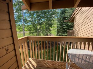 A wooden deck with a metal table and chairs, overlooking a grassy area with trees. - Snow Creek 1553 - Ski-in/ski-out + Pool & Hot Tub (Sun Valley)