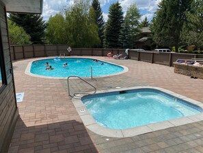 A swimming pool area with two pools, a wooden deck, and a stone wall. - Snow Creek 1553 - Ski-in/ski-out + Pool & Hot Tub (Sun Valley)