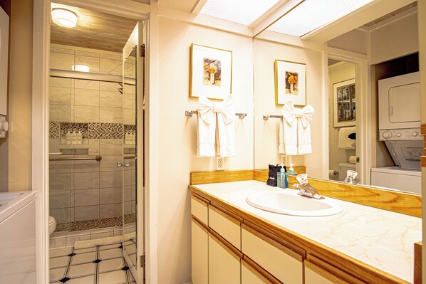 A bathroom with a glass-enclosed shower, a sink with a mirror, and two framed pictures on the wall. - Atelier Escape - Sun Valley Studio + Resort Amenities (Sun Valley)