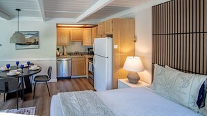 A compact kitchen with wooden cabinets, a refrigerator, and a dining area with a table and chairs. - Atelier Escape - Sun Valley Studio + Resort Amenities (Sun Valley)