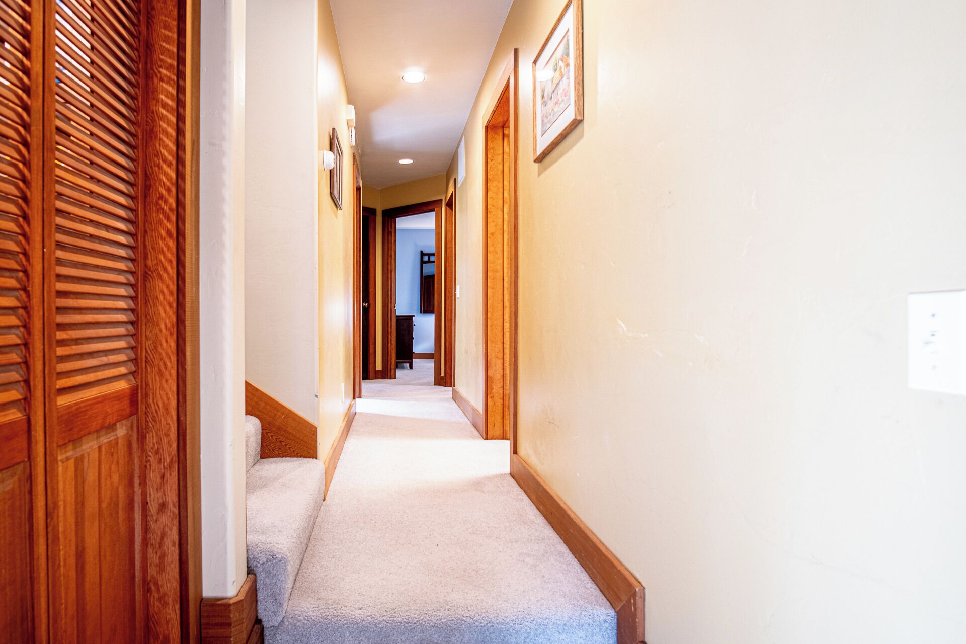 Un pasillo estrecho con puertas de madera y suelo alfombrado.