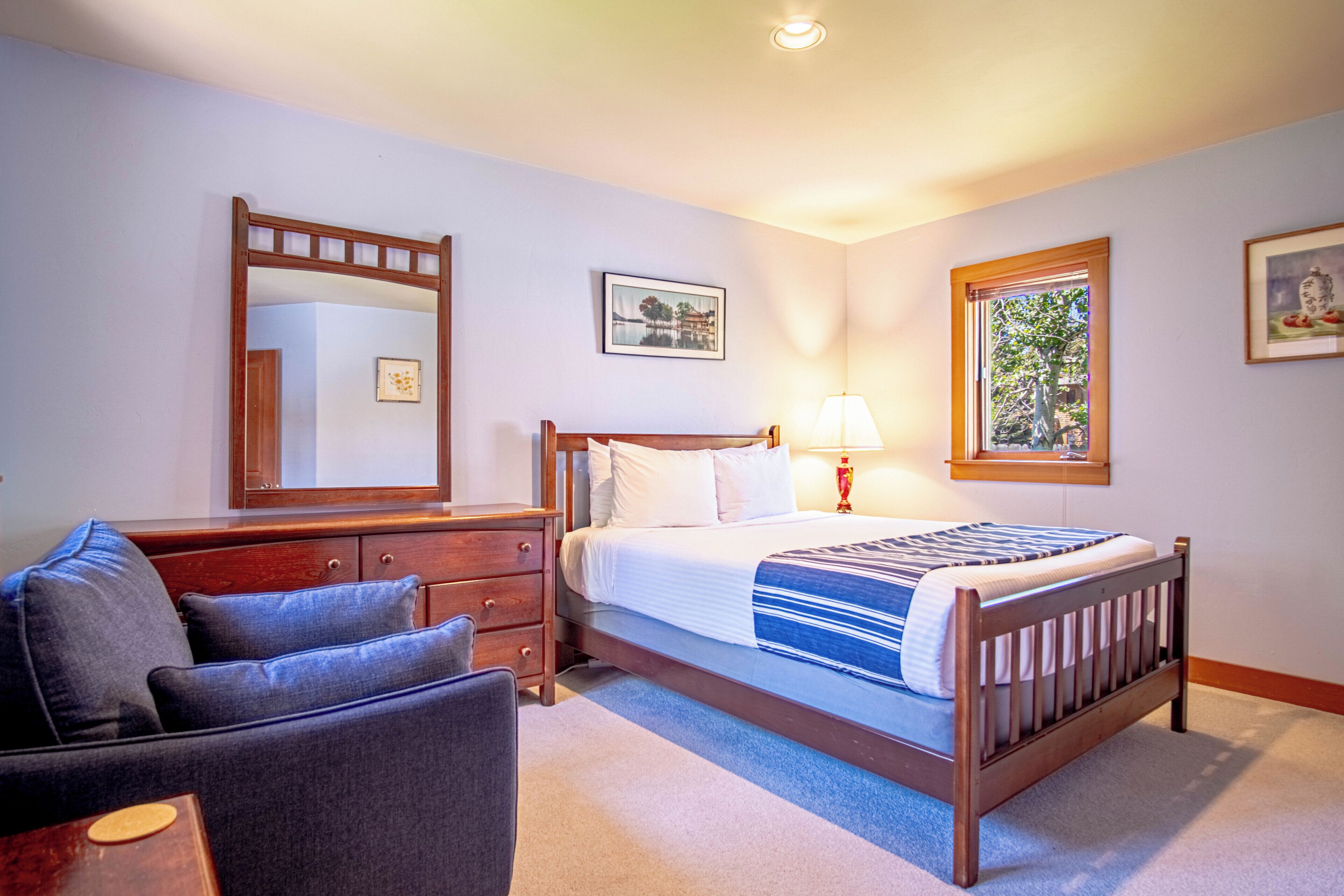 Une chambre à coucher avec un lit, une commode, une chaise, un miroir et une fenêtre.