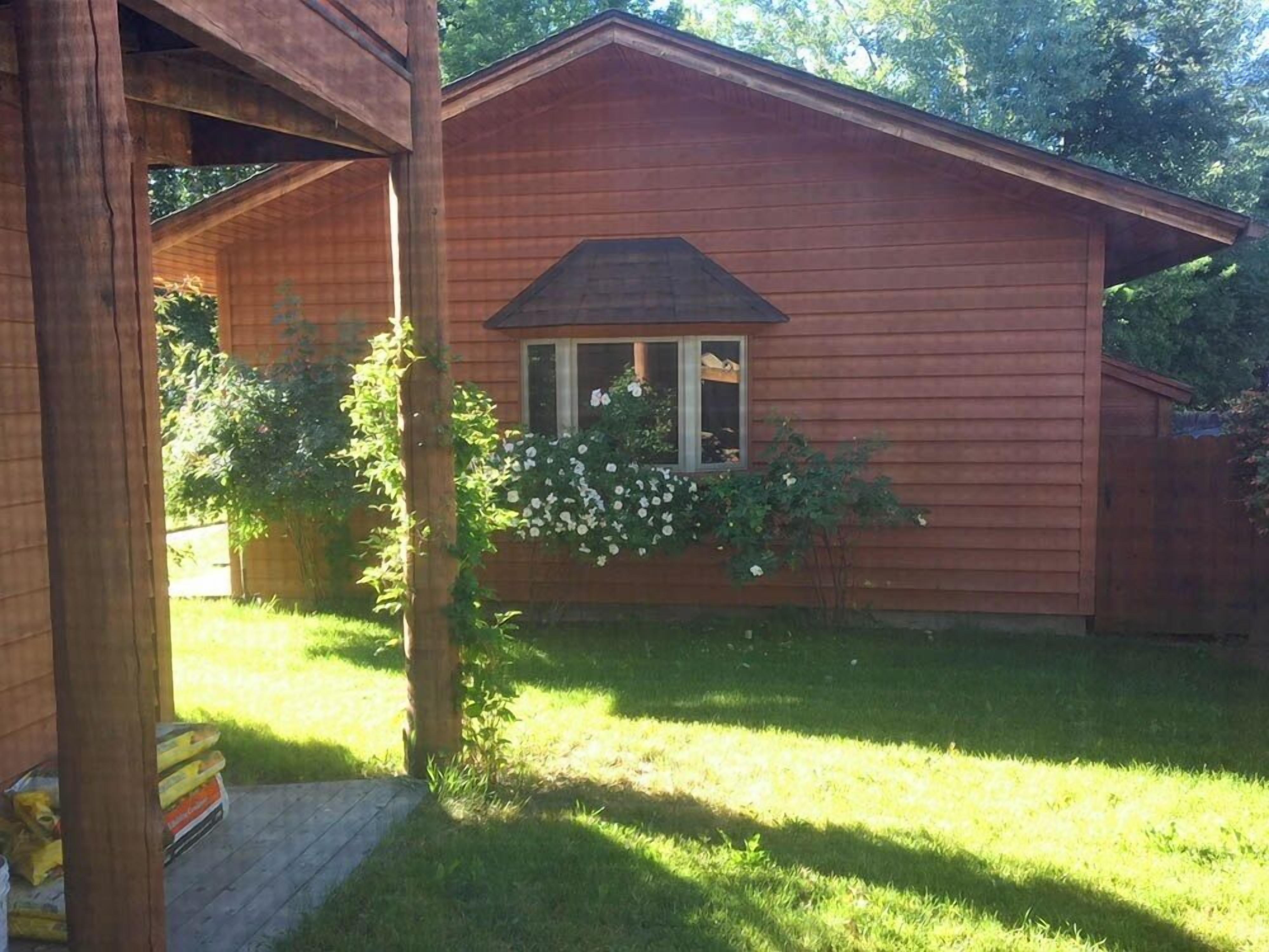 Una cabaña de madera con un ventanal pequeño, rodeada de un patio cubierto de césped y árboles.